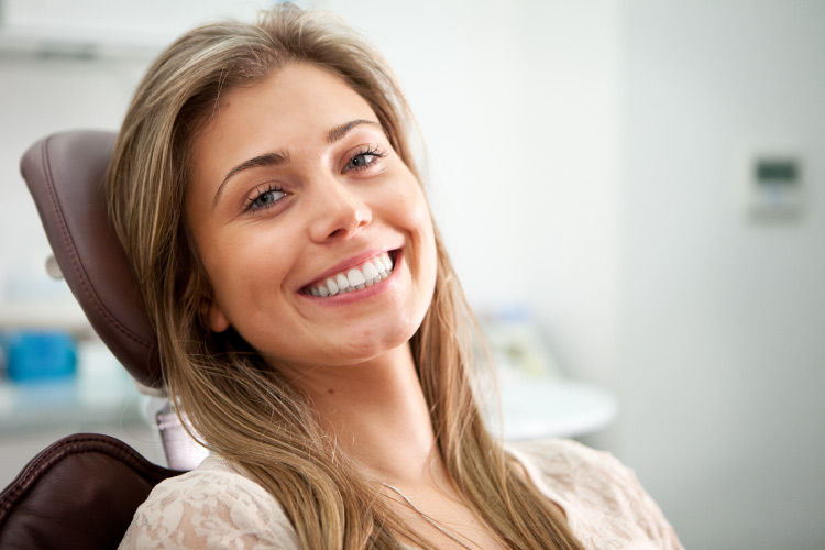 Brunette woman smiles while sitting in a dental chair about to receive root canal therapy to preserve her natural tooth