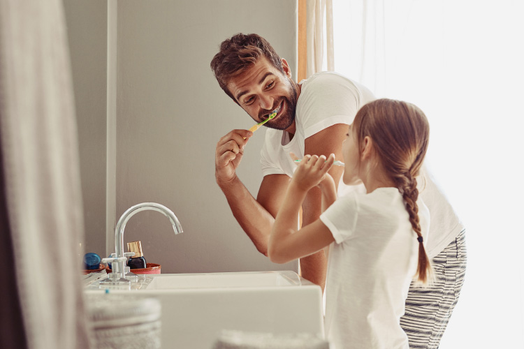 Dad & daughter standing at the sink brushing their teeth