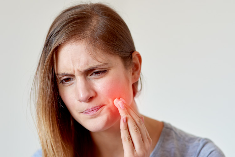 Girl with a pained look holding her hand to her cheek which is radiating red to indicate tooth pain