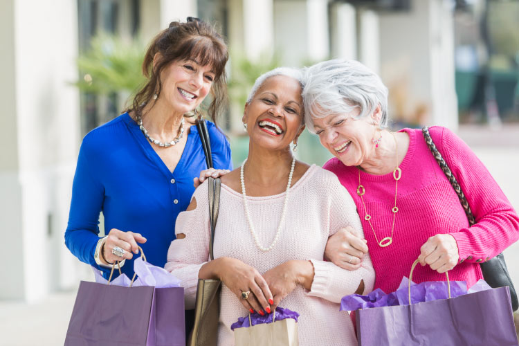 Three smiling mature women walking down the street arm in arm with shopping bags