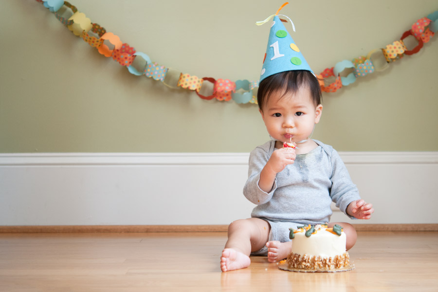 Baby wearing a birthday hat and eating a little cake in front of a paper chain celebrating his first birthday