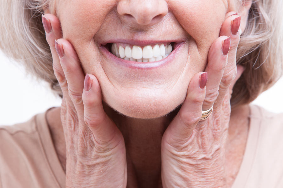 Close up of a mature woman with her hands on her cheeks showing off her new porcelain veneer smile