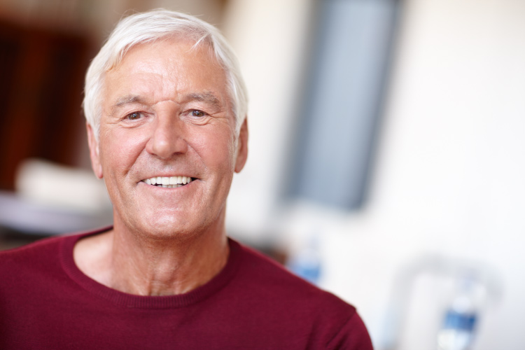 White-haired man with dentures smiles while wearing a red shirt